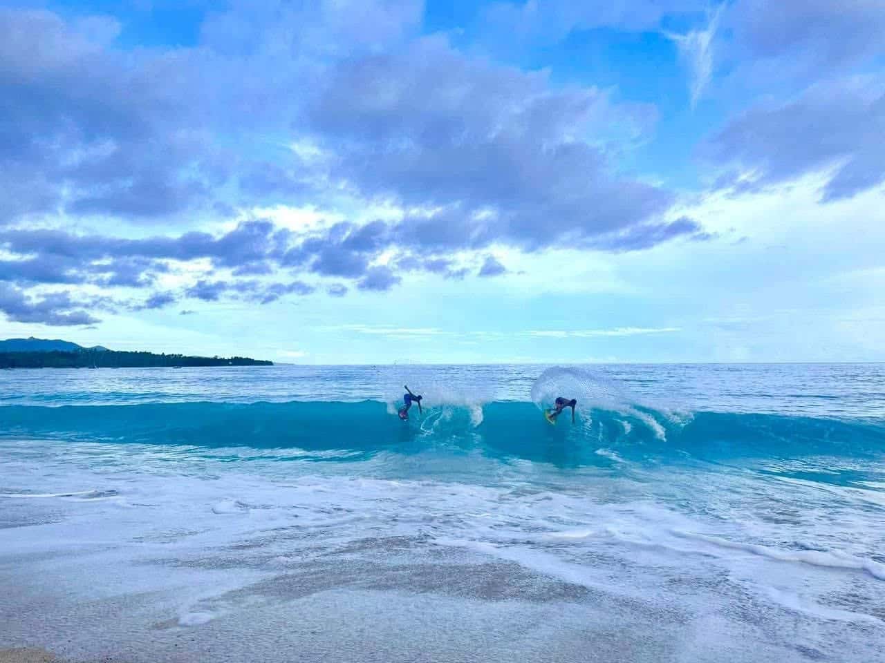 Two surfers catching a wave at beach break in Mati City
