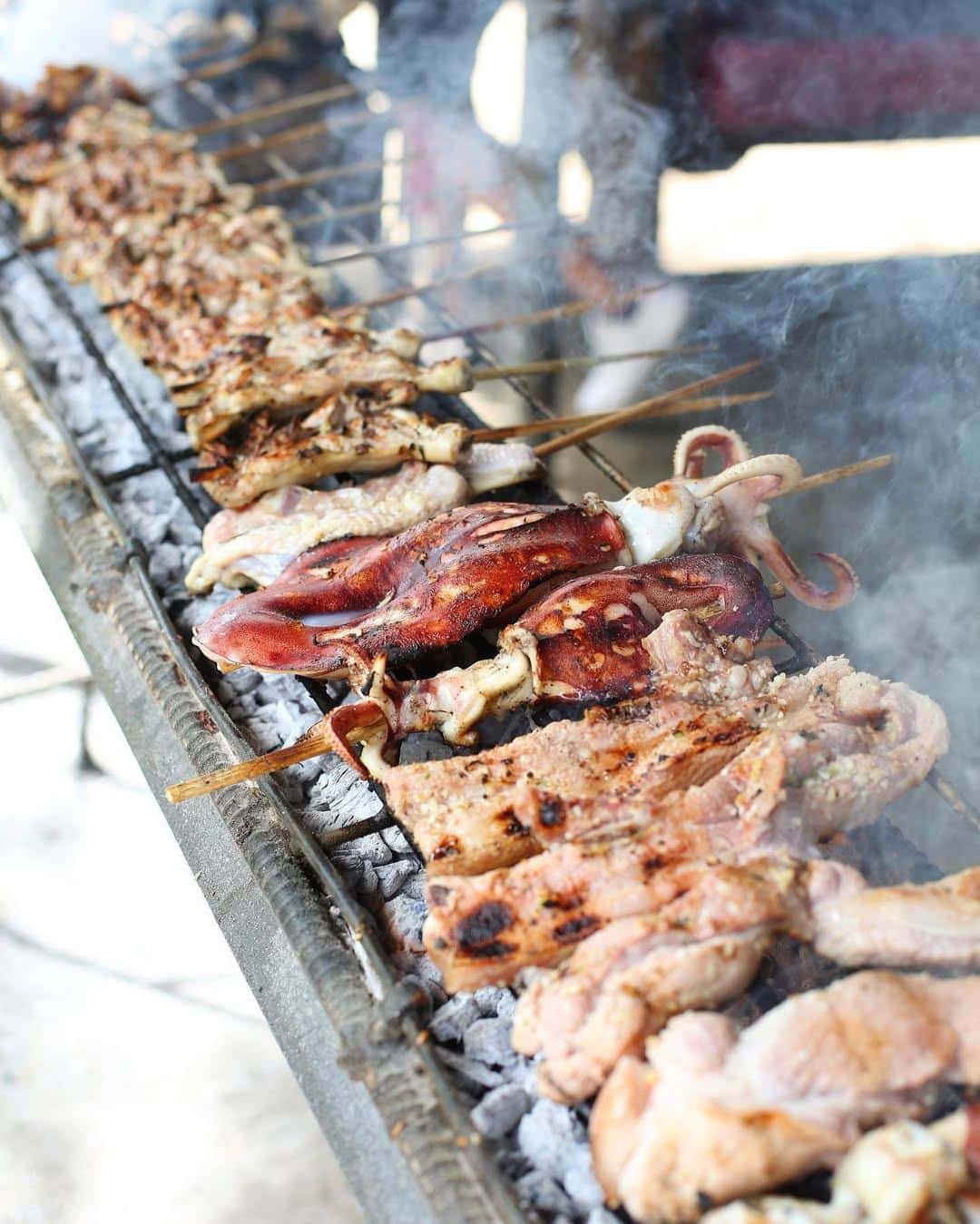 Pork belly and skewers cooking over hot coals