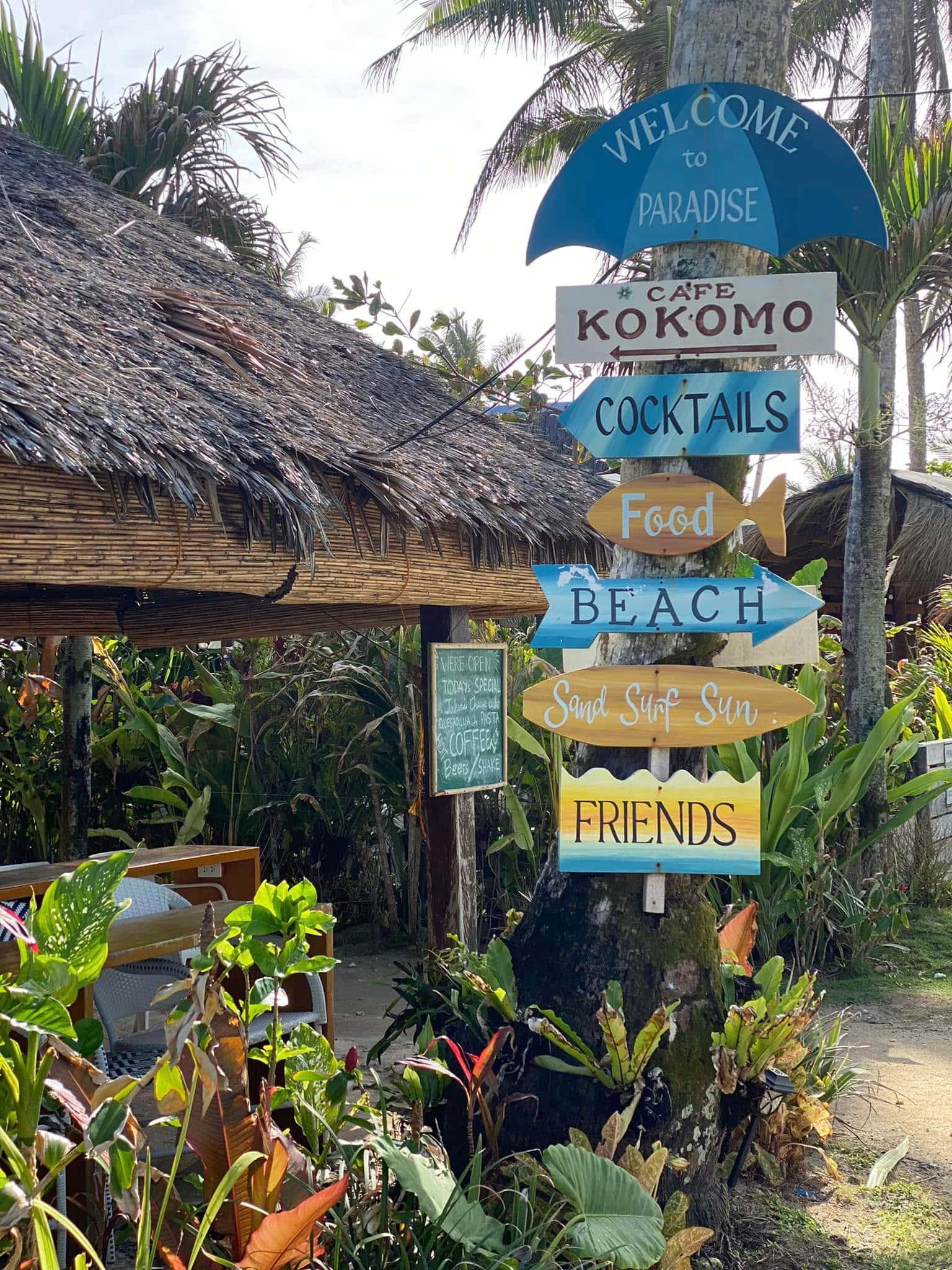 Painted wooden signs pointing to cocktails, food, beach and friends