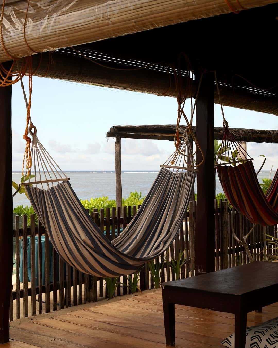 Hammocks strung under a shaded frame facing the sea