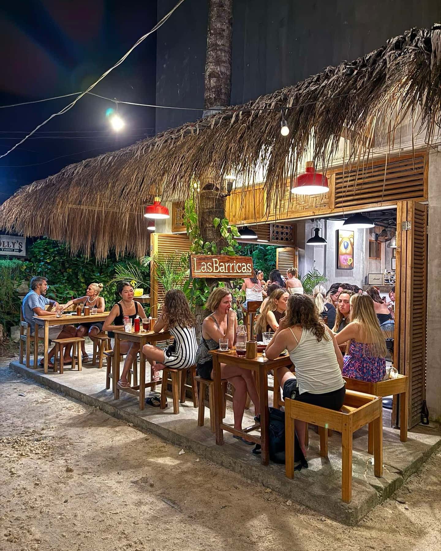 Diners at outdoor tables under a lit thatched roof at night