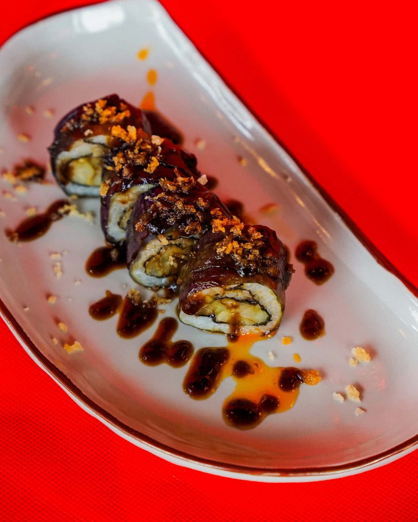 Sushi roll drizzled with dark sauce and crispy topping