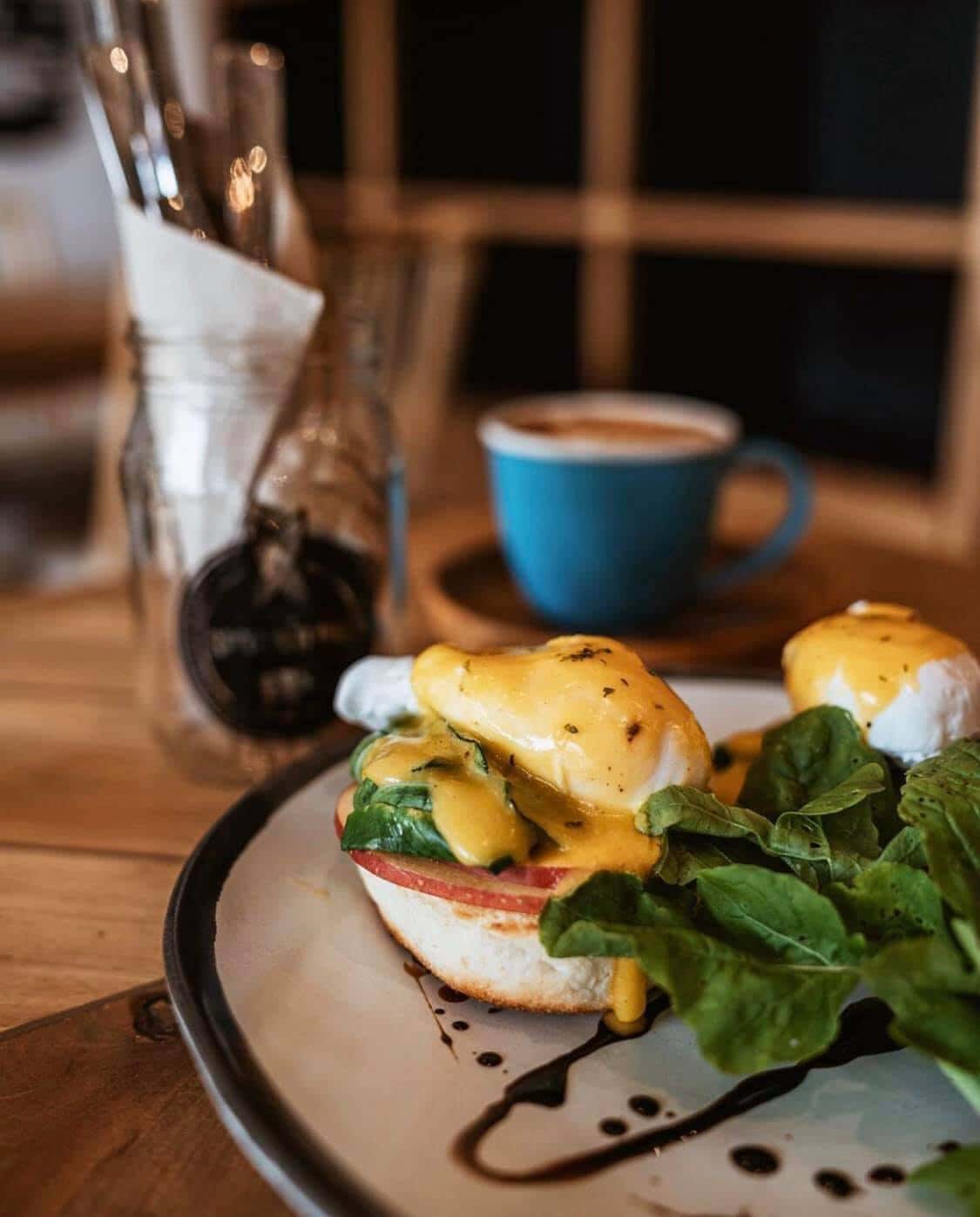 Eggs benedict with spinach beside a cup of coffee
