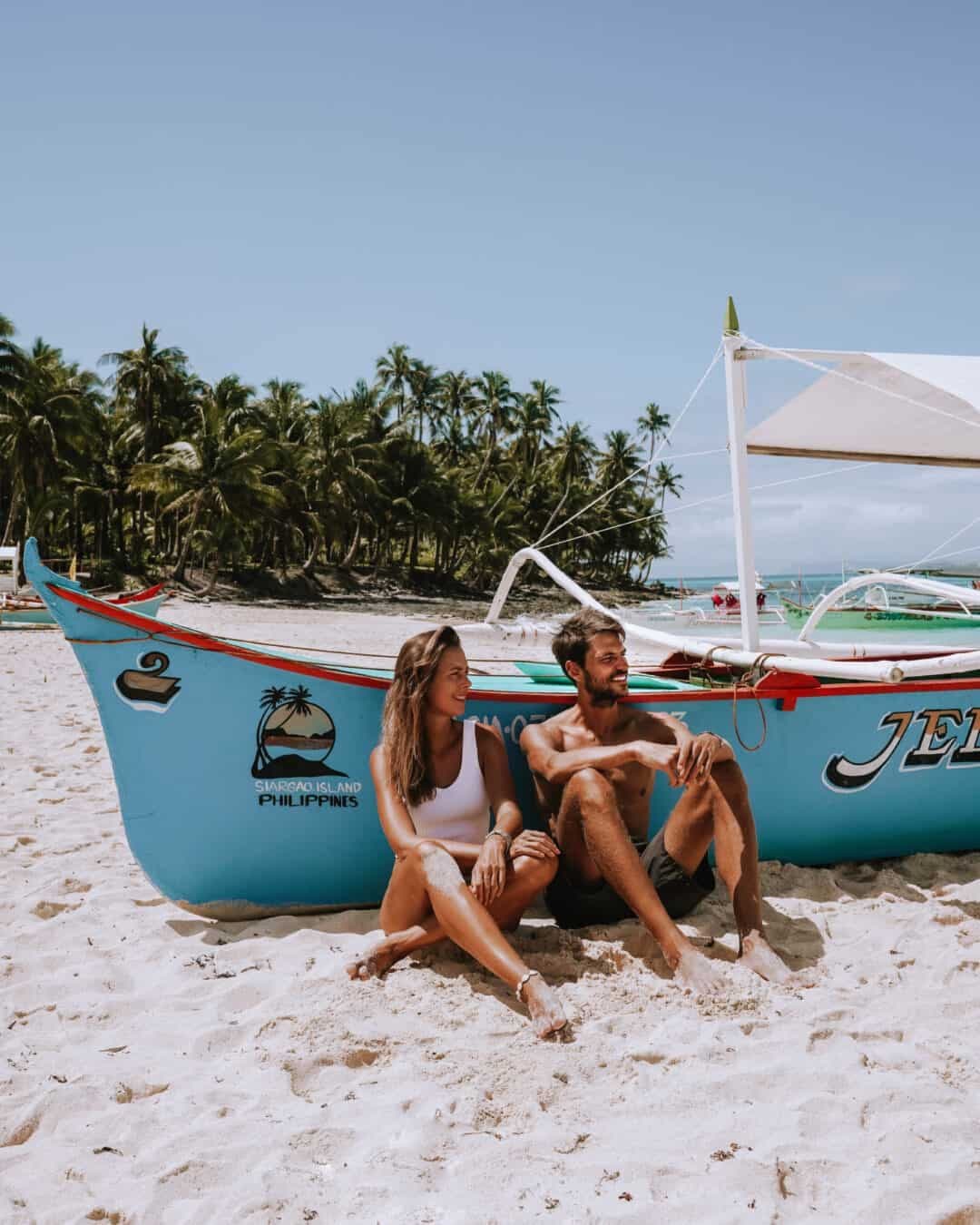 Couple sitting beside a banca boat on the beach at Daku Island, Siargao