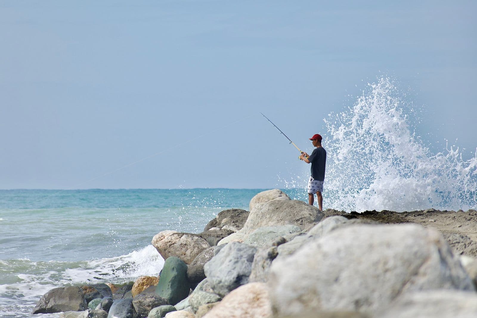A wave breaking on rocks at Agoo, La Union, as a man fishes
