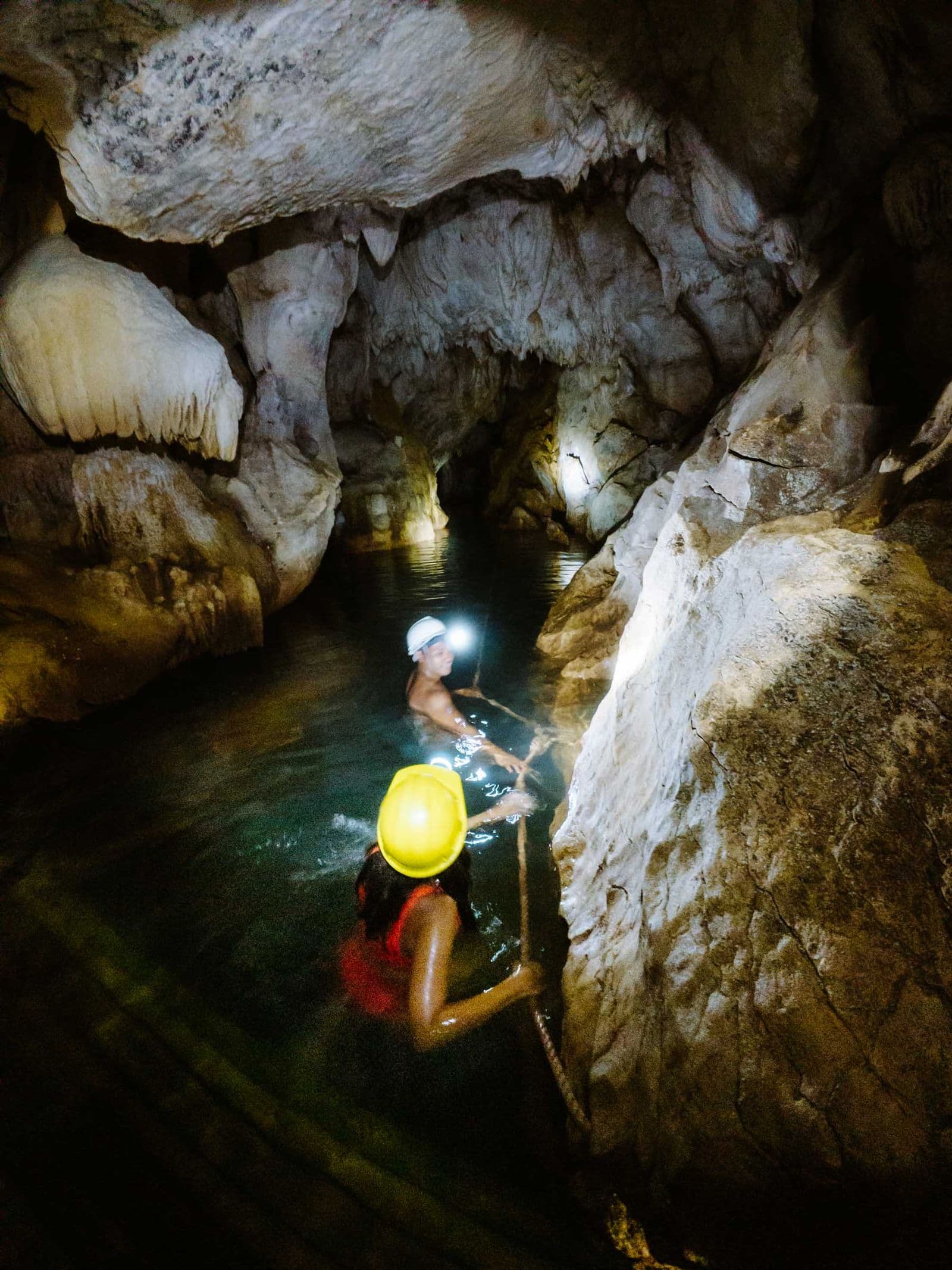Swimmers with headlamps wading through the dark section of Tayangban Cave Pool, Pilar, Siargao